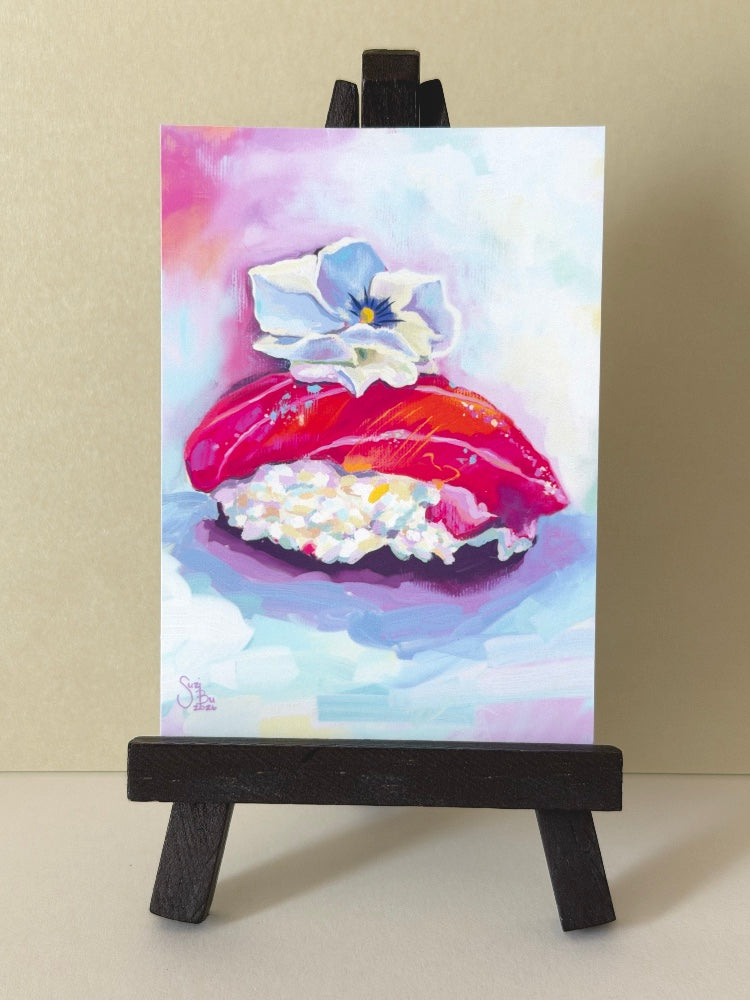 Artistic depiction of sushi with a flower on a small easel against a plain background