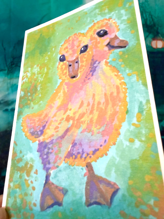 A square art print featuring a colorful, textured painting of a 2-headed duckling in shades of orange, yellow, purple, and green, held at an angle against a dark teal background.